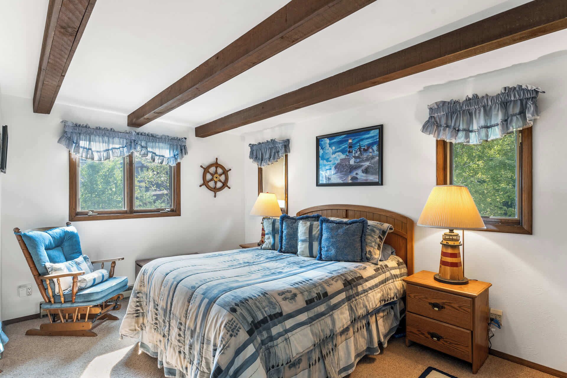 Une chambre à coucher comprenant un lit, deux lampes de chevet, un fauteuil à bascule, une tête de lit en bois et un gouvernail de bateau fixé au mur.