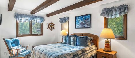 Une chambre à coucher comprenant un lit, deux lampes de chevet, un fauteuil à bascule, une tête de lit en bois et un gouvernail de bateau fixé au mur.