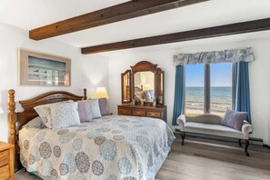 A bedroom with a bed, dresser, mirror, and a view of the sea.