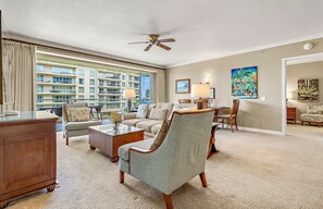 A hotel room with a balcony, a sofa, a chair, a desk, and a ceiling fan.