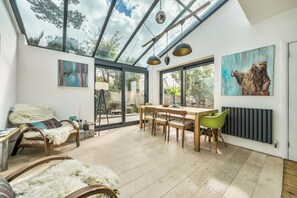 A spacious room with a large glass ceiling, a dining area with wooden furniture, and artwork on the walls.