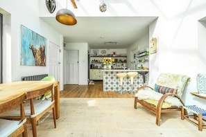 A spacious living area with a wooden dining table, a comfortable armchair, and a view into the kitchen.