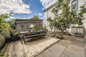 A wooden deck with a bench, surrounded by potted plants and a tree.