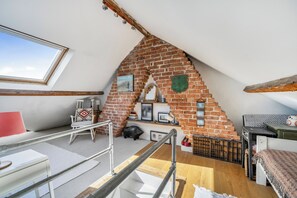 A loft bedroom with a sloped ceiling, exposed brickwork, a skylight, a wooden staircase, and a small piggy bank.