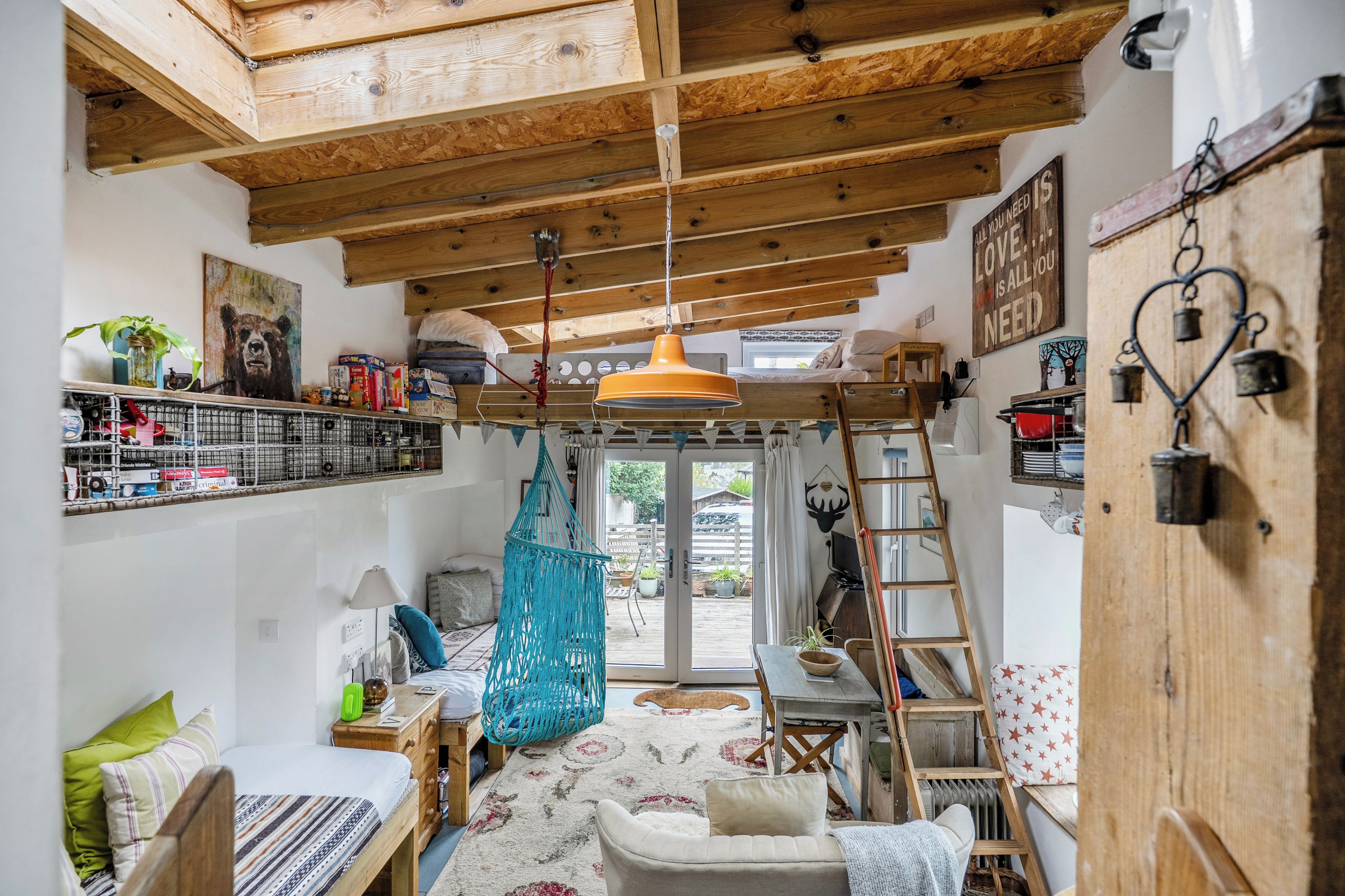 A cozy room with a wooden ceiling, a bed, a desk, and a hammock.