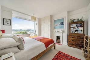 A bedroom with a large bed, a view of the city, a fireplace, and a wooden dresser.