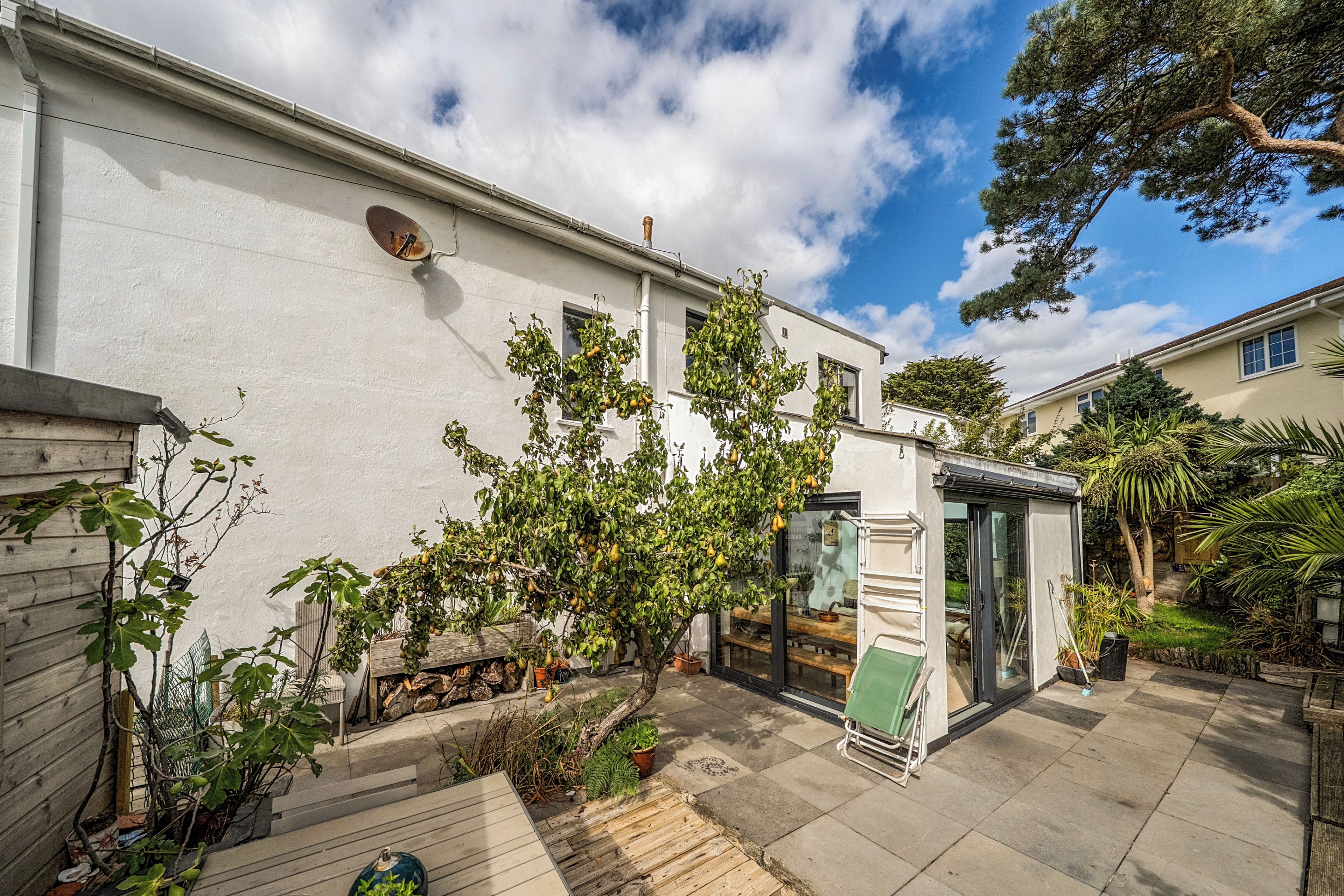 A residential property with a white exterior, a small garden area with potted plants, and a clear sky.