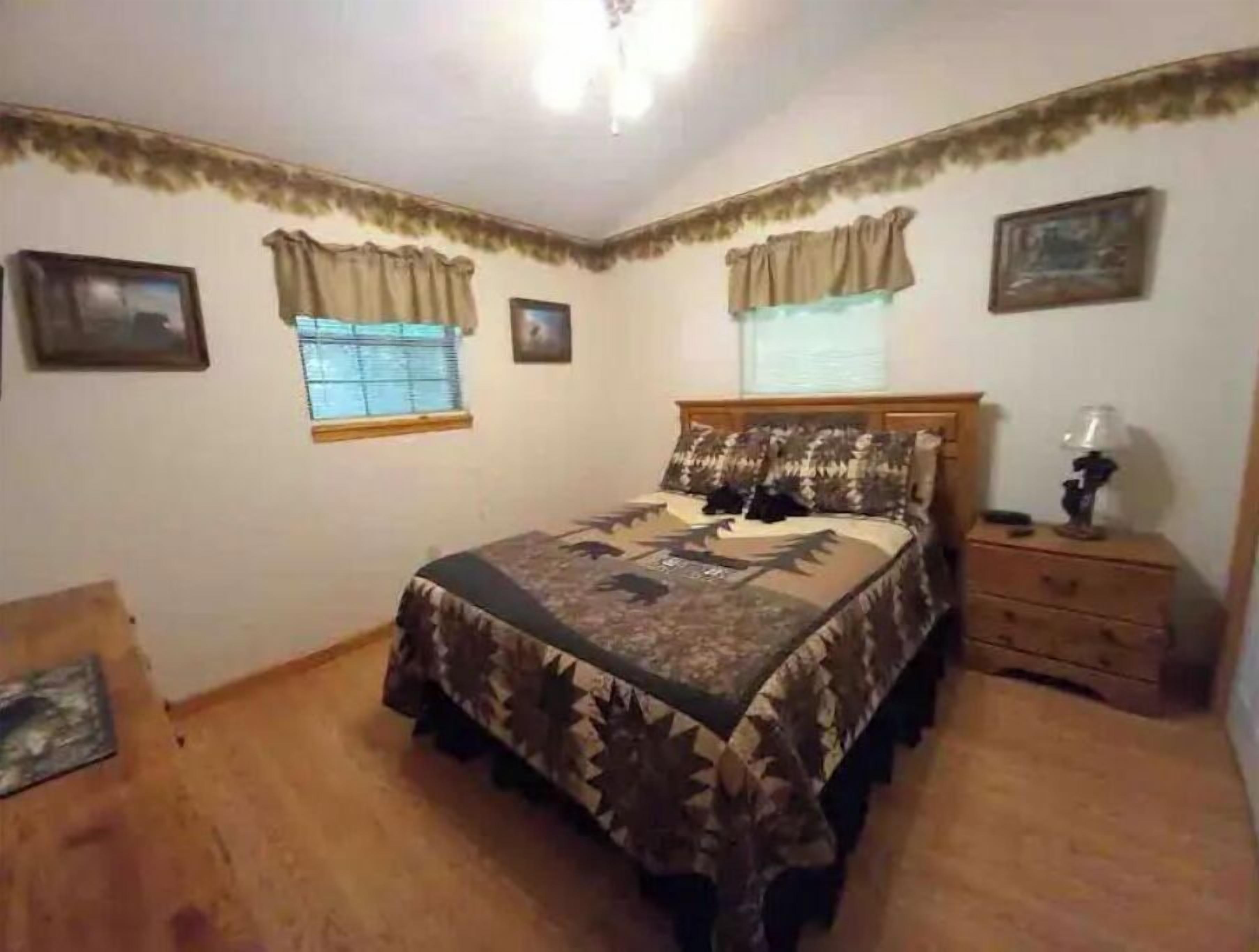 Quarto com cama, mesa de cabeceira, janela com cortinas e luminária no teto.