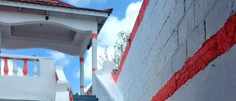 A staircase leading to a building with a red and white facade, a covered area with a red roof, and a clear blue sky in the background.