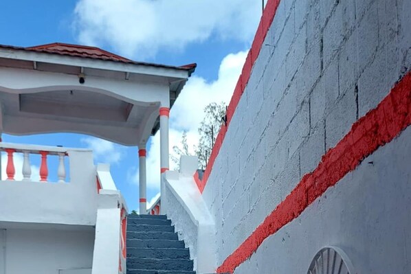 A staircase leading to a building with a red and white facade, a covered area with a red roof, and a clear blue sky in the background.