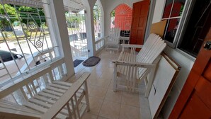 Un espace extérieur abrité, avec des chaises blanches et un sol carrelé.