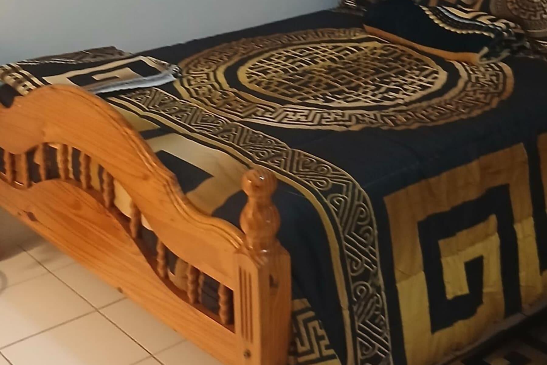 Estructura de cama de madera con cabecera, colcha estampada y cojín decorativo.