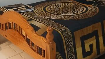 Estructura de cama de madera con cabecera, colcha estampada y cojín decorativo.