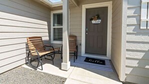 A front porch with a bench and two chairs, a door with a 'welcome' sign, and a doormat. - Retro Caldwell Retreat | Backyard Hammocks | Sleeps 10 (Caldwell)
