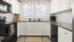 A modern kitchen with white cabinets, a black stove, and a window with decorative curtains. - Retro Caldwell Retreat | Backyard Hammocks | Sleeps 10 (Caldwell)