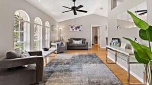 A modern living room with a grey sofa, a coffee table, and a large grey rug. There is a ceiling fan, a world map on the wall, and a large green plant. - Magic Sunrise #417 by Shine Villas (Davenport)
