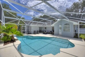 Une piscine extérieure couverte avec un toit en verre, entourée de chaises longues et d’un petit espace salon.