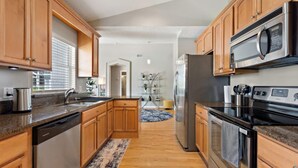 A modern kitchen with wooden cabinets, stainless steel appliances, and a granite countertop. - Magic Sunrise #417 by Shine Villas (Davenport)