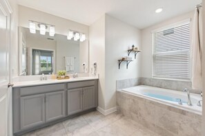 A modern bathroom with a large vanity, a bathtub, and a large mirror. - Fore Play at Champions Gate #419 by Shine Villas (Davenport)
