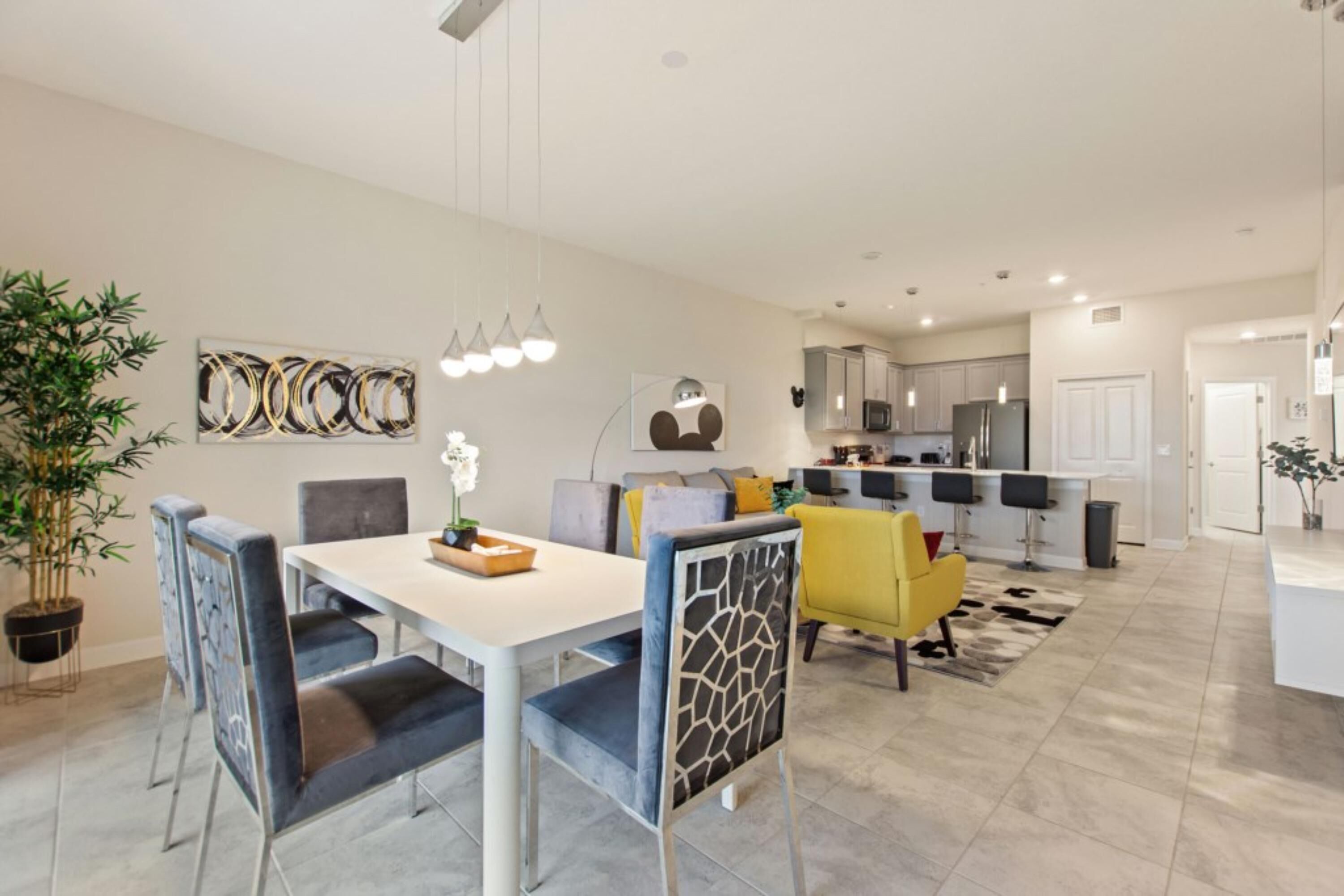 Een moderne keuken met witte kasten, een centraal eiland en een eethoek met een witte tafel en blauwe stoelen.