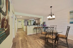 Una cocina amplia con una isla central, un comedor con sillas de metal y un pasillo con piso de madera.