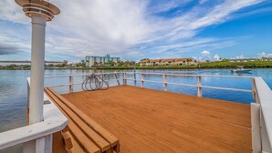 Un pontile in legno con ringhiera, un pilastro bianco e vista su un albergo e edifici dall'altra parte dell'acqua.