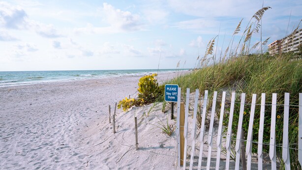 Una spiaggia con un cartello che recita: 'PER FAVORE NON CAMMINARE SULLE DUNE'.