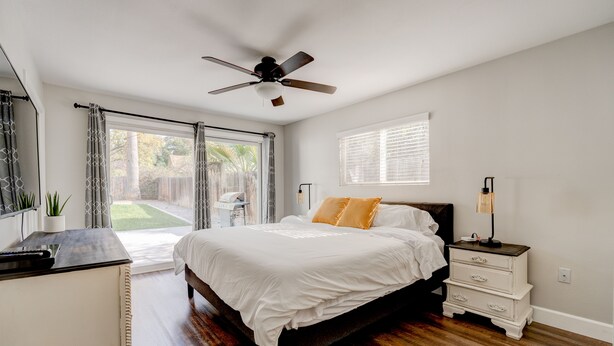 A bedroom with a bed, a ceiling fan, a bedside table, a nightstand, and a window.