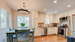 A kitchen with white cabinets, a wooden dining table, and a chandelier.