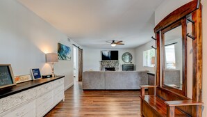 A spacious living room with hardwood flooring, a large wooden bench, a white dresser, and a stone fireplace.