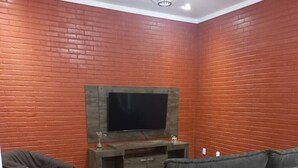 Een woonkamer met een bakstenen muur, een flatscreen televisie bevestigd aan een houten dressoir, en een grijze modulaire bank.