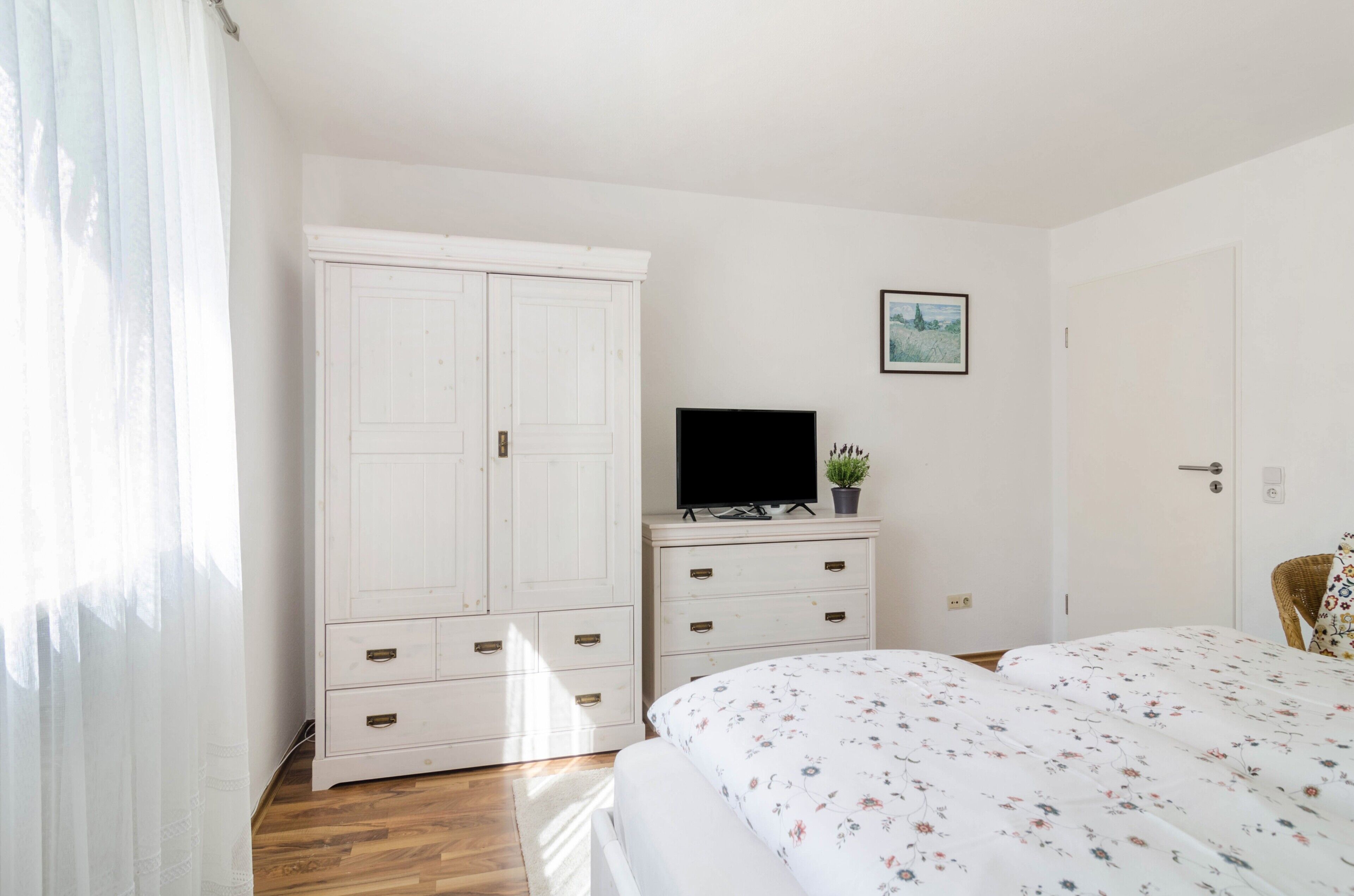 Une chambre à coucher avec un lit, un téléviseur posé sur une commode, une armoire et une porte.