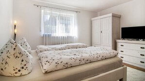 Quarto com cama, guarda-roupa, televisão e janela com cortinas.