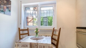 Uma área de refeições com uma mesa posta para dois, uma janela com vista para o verde e uma cozinha com fogão.