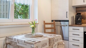 Uma cozinha com mesa posta para dois, uma cafeteira e uma janela com vista para o verde.