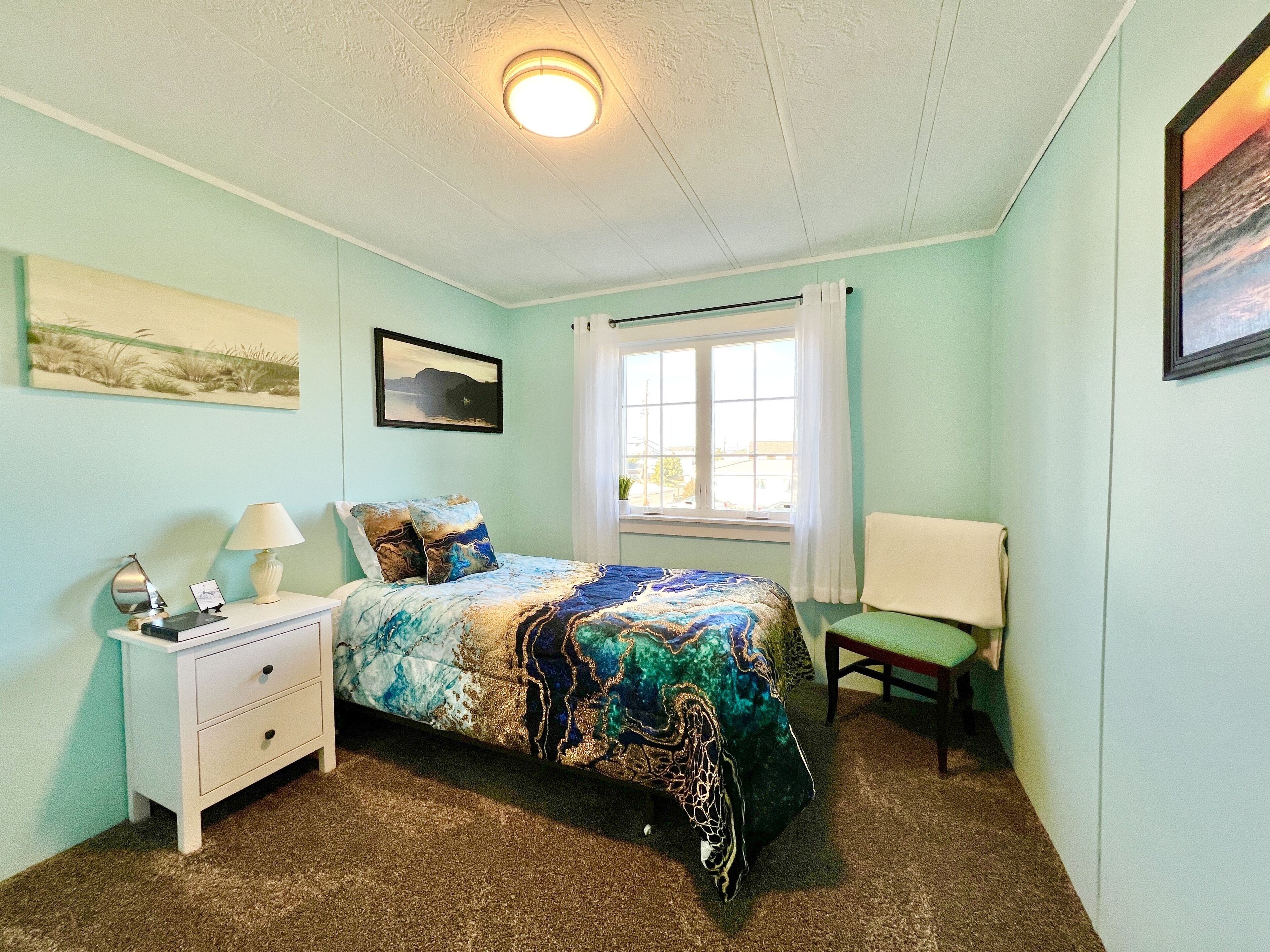 A bedroom with a bed, a nightstand, a chair, a window with curtains, and a ceiling light.