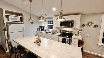 A modern kitchen with a large island, stainless steel appliances, pendant lighting, and a view to the dining area.
