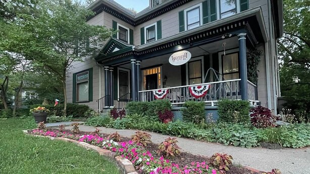 A two-story building with a porch decorated with holiday garlands. - Loganberry Inn (Fulton)