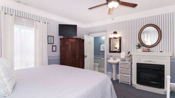 A bedroom with a bed, a ceiling fan, a television, a fireplace, and a bathroom visible through an open door.