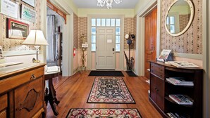 A hallway with a chandelier, a wooden desk, a mirror, and a door with a window. - Loganberry Inn (Fulton)