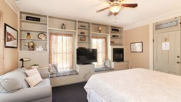 A bedroom with a large bed, a television, built-in shelving, a ceiling fan, and a door with a lock.