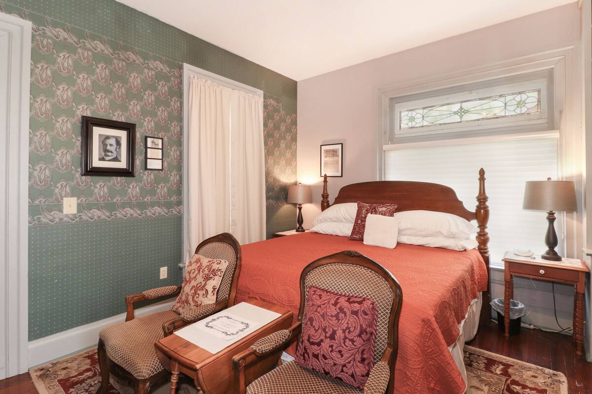 A bedroom with a large bed, two chairs, a small table, and a window with a view.