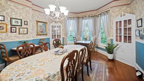 A dining room with a large table, chairs, and a chandelier. There are framed pictures on the walls and a window with curtains. - Loganberry Inn (Fulton)