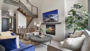 A modern living room with a fireplace, a large painting of a mountain, and a staircase.