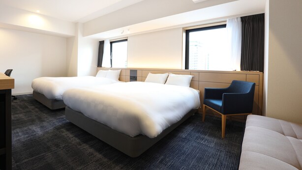 Habitación de hotel con dos camas, un escritorio, una silla y un ventanal con cortinas.