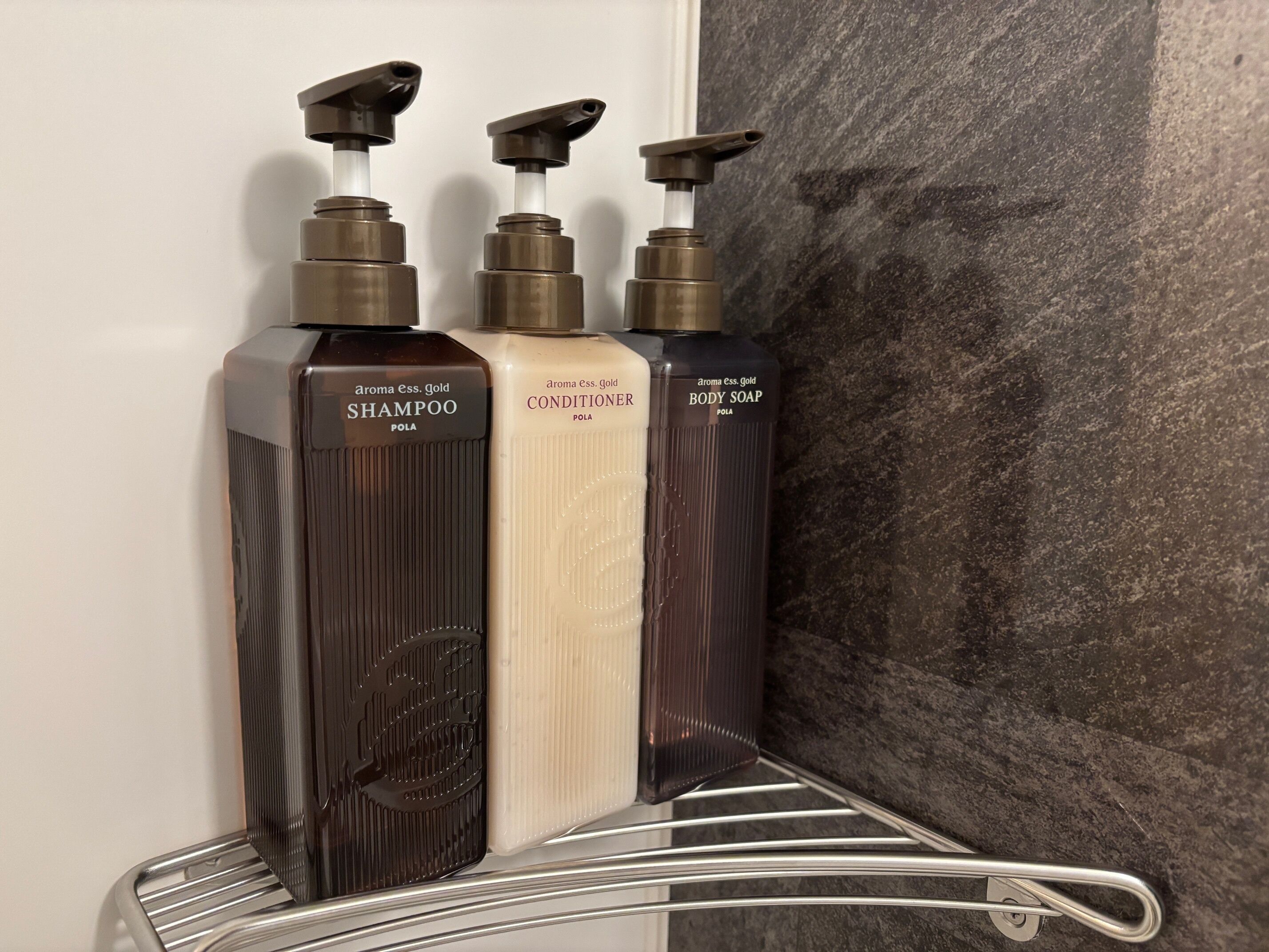 Três frascos de produtos de higiene pessoal em uma prateleira de metal em um banheiro.