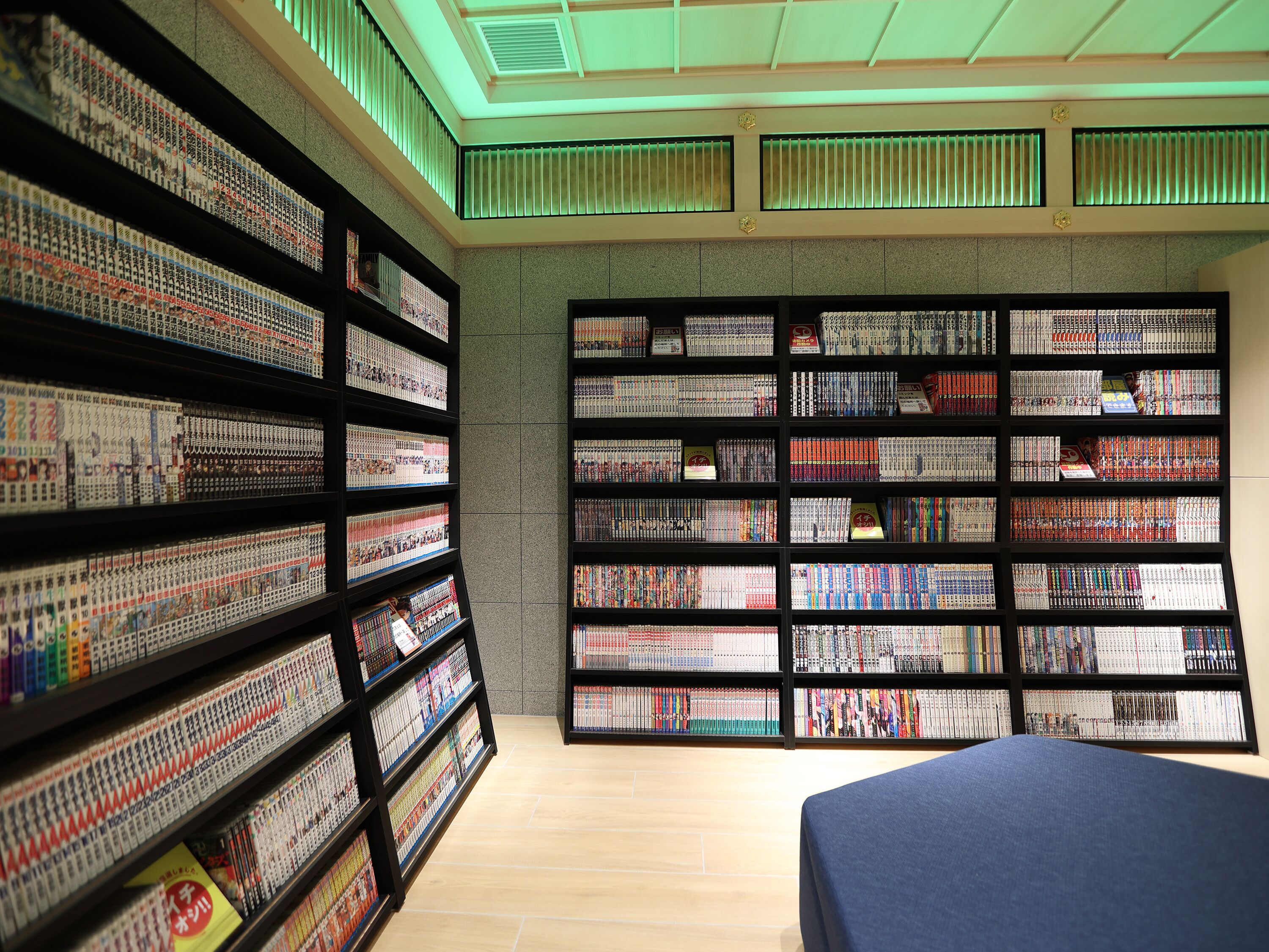 A library with bookshelves filled with books, a blue sofa, and a ceiling with green lighting.