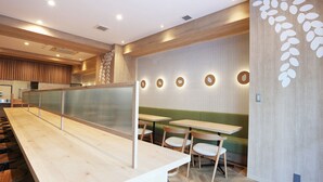 Un interior de restaurante moderno con una larga barra de madera, varias mesas con sillas y una pared decorativa con diseños circulares.