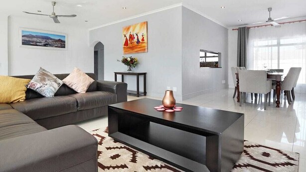A modern living room with a sectional sofa, a coffee table, and a dining area with a table and chairs.