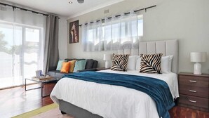 A modern bedroom with a large bed, a sofa, a desk, and a window with curtains.